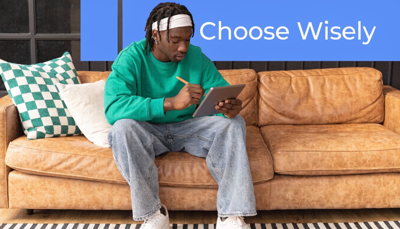 A young man with locs sitting on a brown leather couch using a digital tablet and stylus.