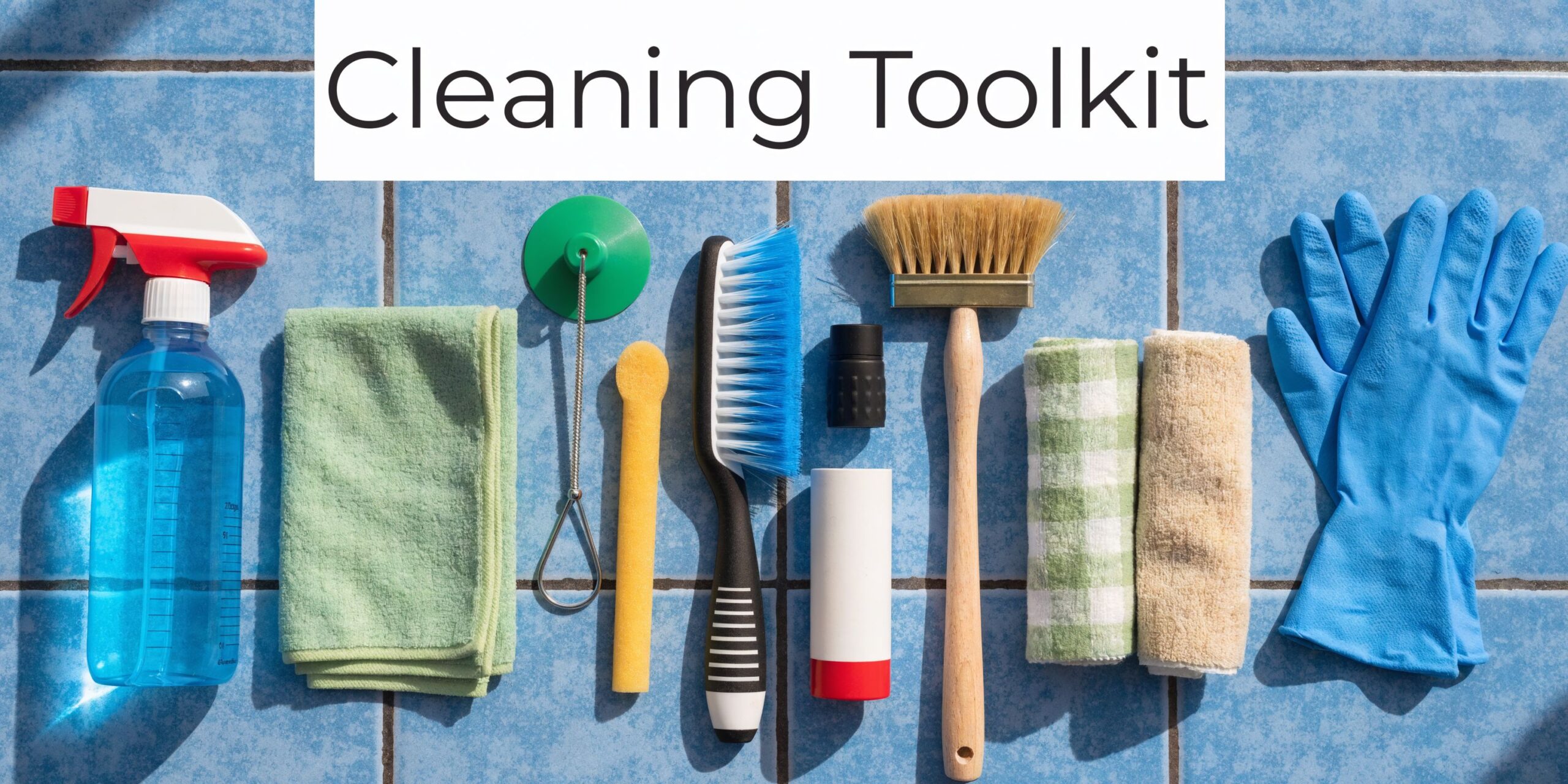 An organized flat lay of various household cleaning supplies and tools arranged on blue tiled flooring.